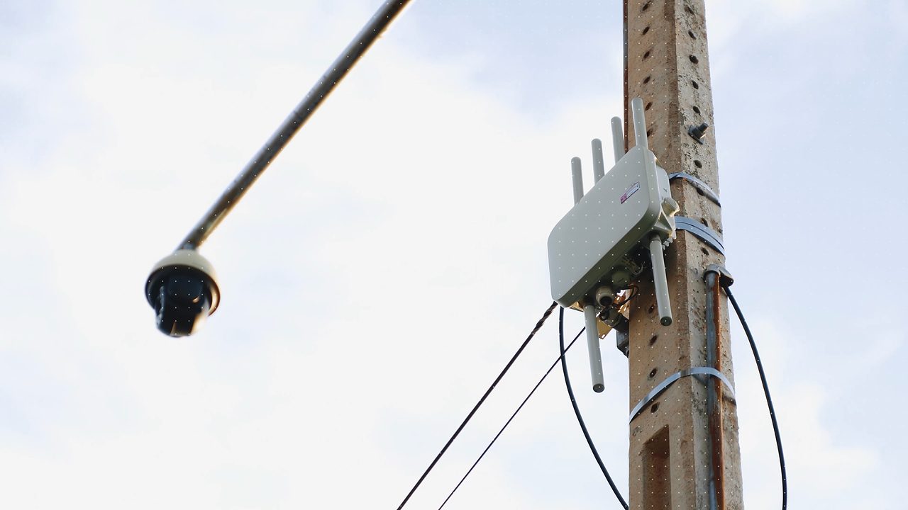 Ponto de acesso de Wi-Fi público instalado em poste, ao lado de uma câmera